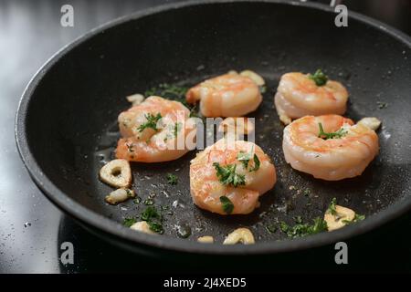 Garnelen in einer Pfanne mit Knoblauch und Petersilie in Olivenöl auf dem Herd gebraten, Kochen eine köstliche Vorspeise, Kopierer Platz, ausgewählte Fokus, enge Tiefe f Stockfoto