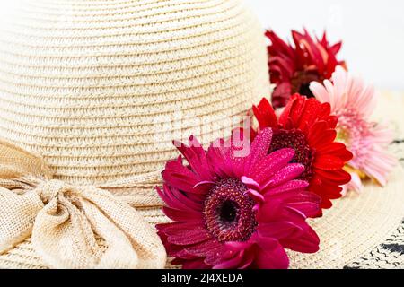 Damen-Sonnenhut mit roten Gänseblümchen und Jute-Schleife auf weißem Hintergrund Stockfoto