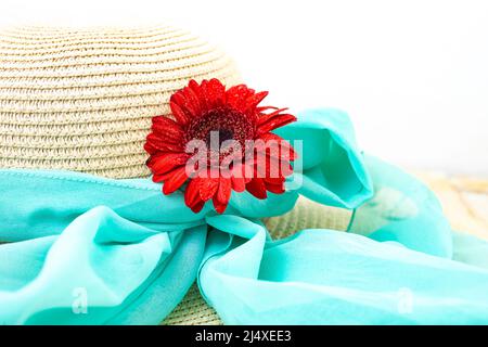 Rote Gerbera Gänseblümchen Blume auf einem Strohhut mit einem blauen Schal gebunden, Sommer, Strand, romantischen Hintergrund Stockfoto