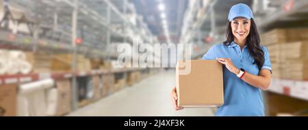 Junge Frau in Arbeitskleidung vor einem riesigen Lager, die Pappkarton für die Lieferung an den Kunden hält. Stockfoto