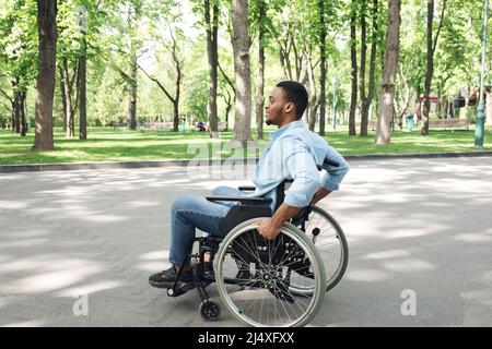 Seitenansicht des jungen schwarzen Mannes im Rollstuhl, der Zeit im Stadtpark verbringt, in voller Länge Stockfoto