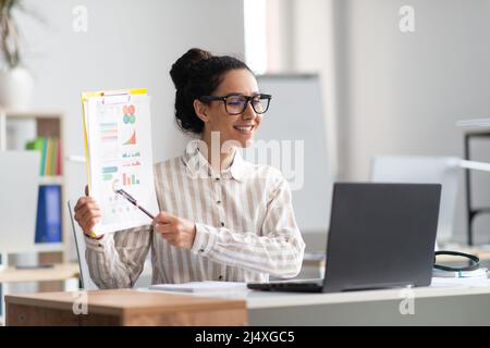 Telearbeitskonzept. Glückliche weibliche Managerin, die einen Videoanruf auf dem Laptop führt, eine virtuelle Präsentation vorführt und lächelt Stockfoto