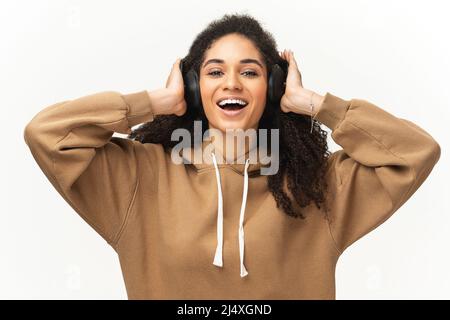 Entzückende Frau im legeren Hoodie, die schnurlose Kopfhörer zum Musikhören verwendet, Teenager im Kopfhörer, die ihre Lieblingstitel genießen und auf blauem Hintergrund isolierte Hörbücher hören Stockfoto
