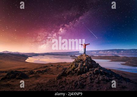 Der Reisende Mann trägt rote Kleidung und hebt den Arm und steht auf dem Berg mit milchiger Straße im Baikalsee, Sibirien, Russland. Stockfoto