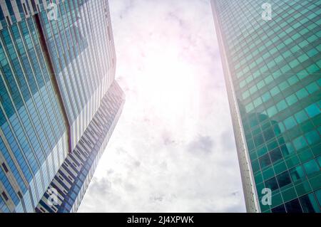 Ein Blick von UNTEN AUF die GIPFEL der WOLKENKRATZER UND WOLKEN AM HIMMEL, das KONZEPT DES MODERNEN STÄDTISCHEN BÜROBAUS, ein neues modernes Gebäude. Stockfoto