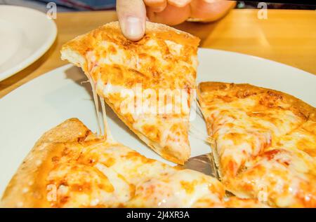Nahaufnahme der Finger, die ein Stück heiße traditionelle italienische Pizza mit geschmolzenem Käse halten. Stockfoto