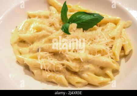 Draufsicht auf das traditionelle italienische Gericht Penne Pasta mit geriebenem Käse und Basilikum. Stockfoto