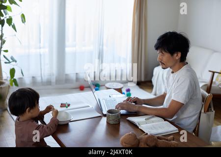 Japanischer Mann, der von zu Hause aus mit Kind arbeitet Stockfoto