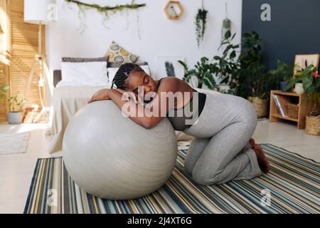 Junge, schwanger Frau, die sich während der Wehen an einem Fitnessball lehnt und an Schmerzen leidet Stockfoto