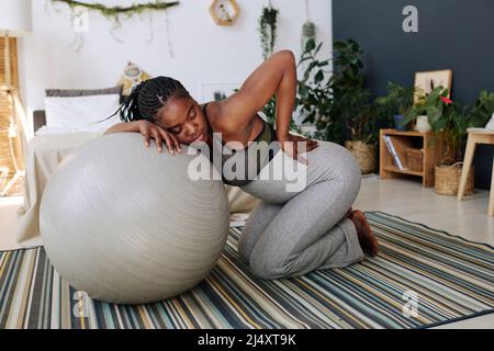 Afrikanisches, schwanger Mädchen mit Schmerzen, das sich während der Wehen im Zimmer auf den Fitnessball lehnte und die Augen geschlossen hatte Stockfoto