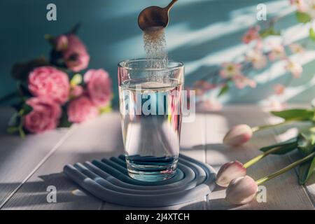 Kollagenpulver wird mit einem Löffel in ein Glas Wasser gegeben Stockfoto