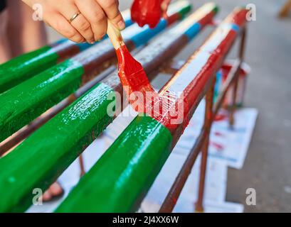 Pinsel in der Hand malt eine Bank in hellen Farben, Malerei eine Gartenbank, auf der Straße Stockfoto