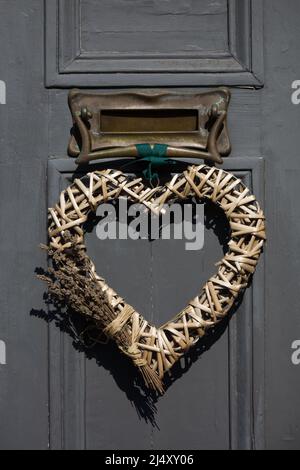 Love Heart förmigen Korbkranz Türdekoration auf einer dunkelgrau bemalten Haustür mit Messing Briefkasten in einem englischen Dorf im Frühjahr Stockfoto