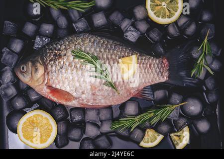 Kochen von Fisch, rohem Fisch auf einem Backblech mit Eiswürfeln, Zitronenscheiben und Rosmarinzweigen Stockfoto