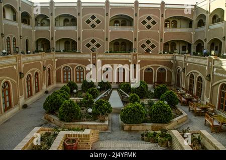 Yazd, Iran, 19. Feb 2021: Blick auf den Kellerhof mit Nadelsträuchern und Wasserbecken mit Tischen und Stühlen im alten DAD-Hotel in Yazd. Stockfoto