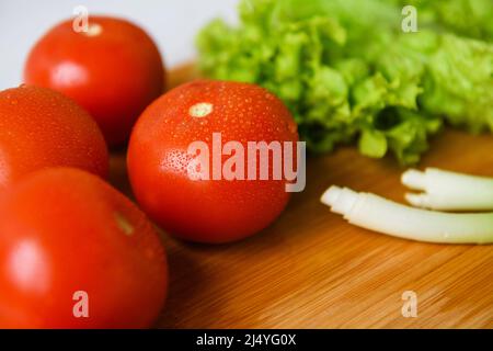 Frisches Gemüse für Salat liegt auf einem Holztisch mit Schneidebrett. Nahaufnahme. Stockfoto