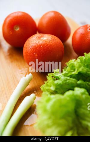 Frisches Gemüse für Salat liegt auf einem Holztisch mit Schneidebrett. Nahaufnahme. Stockfoto