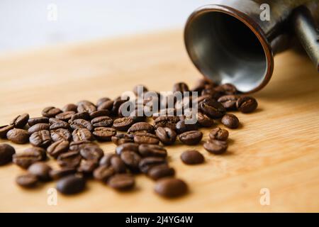 Nahaufnahme einer Streuung von Kaffeebohnen auf einem Holzbrett mit einem Cezve im Hintergrund Stockfoto