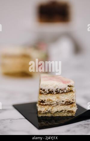 Scheibe Tiramisu-Bento-Kuchen. Präsentation des Kuchens im Abschnitt. Süßes Dessert für eine Person. Kleiner Geburtstagskuchen. Hintergrund von anderen Bento-Kuchen Stockfoto