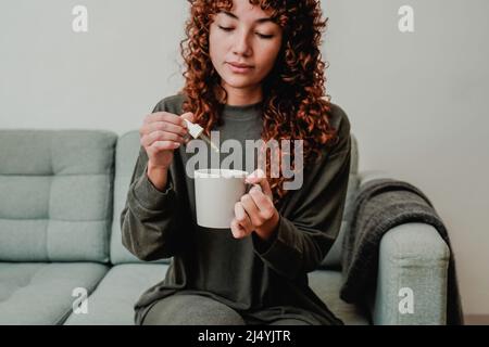 CBD-Hanföl - Frau, die Cannabisöl in einer Teetasse nimmt - Fokus auf die Hand, die Tropf hält Stockfoto