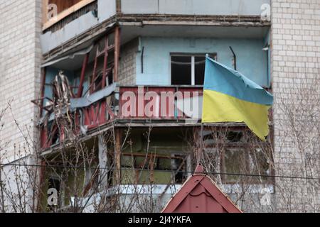 BORODIANKA, UKRAINE - 16. APRIL 2022 - Eine ukrainische Flagge fliegt vor einem Wohngebäude, das durch den Beschuss des russischen Tr beschädigt wurde Stockfoto