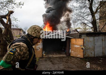 Charkiw, Ukraine. 18. April 2022. Ein ukrainischer Soldat geht nach einem russischen Artillerieangriff in Charkiw vor eine brennende Garage. Nach der russischen Konzentrationsoffensive im Osten der Ukraine ist Charkow, die zweitgrößte Stadt der Ukraine, nun ständig von russischen Bombardierungen und Luftangriffen bedroht. Kredit: SOPA Images Limited/Alamy Live Nachrichten Stockfoto