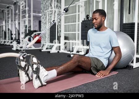 Porträt eines afroamerikanischen jungen Mannes, der in der Physiotherapie-Klinik im Fitnessstudio Rehabilitationsübungen macht, Kopierraum Stockfoto