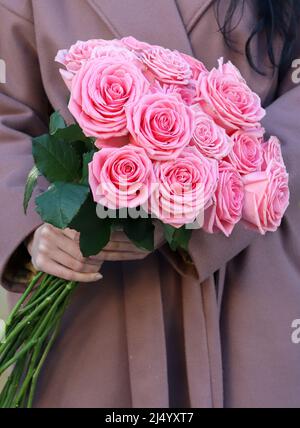 Schönes mono Bouquet von rosa Rosen. Frau in braunem Mantel mit Rosenstrauß. Stockfoto