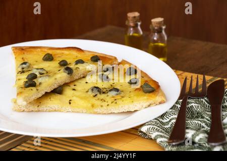 Zwei Scheiben Kaperpizza auf einem weißen Teller mit Besteck an der Seite Stockfoto