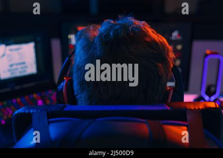 Silhouette des Rückens eines jungen Mannes, der süchtig nach Videospielen ist, die auf einem Computer mit Kopfhörern spielen. Stockfoto