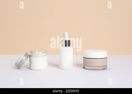 Creme in einem Glas, Serumflasche und Gesichtsmaske oder Peeling auf neutralem beige-weißen Hintergrund. Natürliche Hautpflege kosmetische Produkte, Mockup. Stockfoto