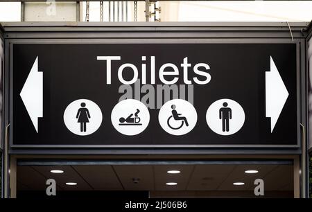 Großes Schild mit schwarzen und weißen Toiletten über dem Kopf mit Symbolen für männliche, weibliche, behinderte und Baby-Wickelnde. Stockfoto