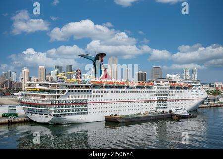Ecstasy der Carnival Cruise Line, die am Hafen von Miami mit der Skyline von Miami im Hintergrund angedockt ist. Stockfoto