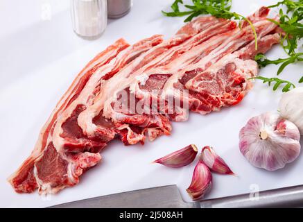 Rohe Lammkoteletts auf dem Küchentisch mit Knoblauch, Rucola, Gewürzen Stockfoto