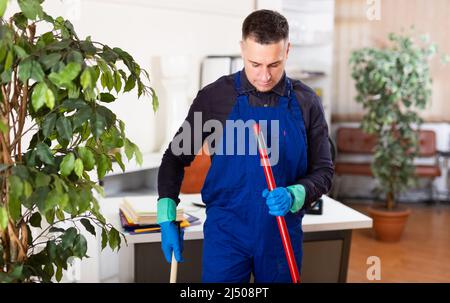 Männlicher professioneller Hausmeister, der im Büroinneren Staub staubt Stockfoto