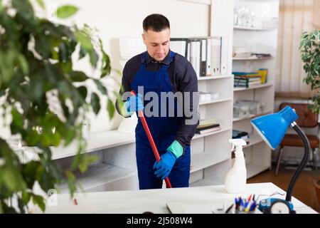 Männlicher professioneller Hausmeister, der im Büroinneren Staub staubt Stockfoto