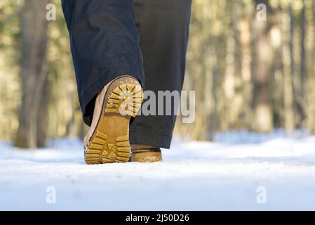 Frau, die im Winterwald auf Schnee läuft. Konzentrieren Sie sich auf die Sohle der Show mit Schnee. Stockfoto
