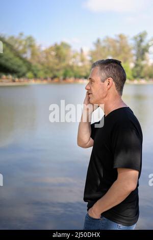 Reifer Geschäftsmann, der an einem See mit dem Handy telefoniert Stockfoto