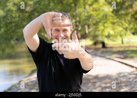 Ein hübscher reifer Mann schaut durch einen Rahmen aus Händen. Attraktive Mann machen Bild für Finger, isoliert auf unscharfen Hintergrund mit Kopierraum für te Stockfoto