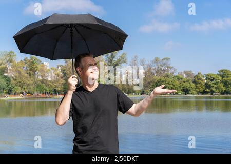 Kaukasischer Mann mit Regenschirm an einem sonnigen Tag, zu sehen, dass es nicht regnet. Fehldiagnosekonzept Stockfoto