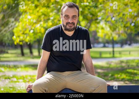 Porträt eines reifen bärtigen Mannes, der in einem Park sitzt und die Kamera anschaut Stockfoto