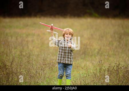 Kind Spaß mit Spielzeug Flugzeug im Feld. Kleiner Junge mit Holzflugzeug, Junge will Pilot und Astronaut werden. Glückliches Kind spielen mit Spielzeug Flugzeug Stockfoto