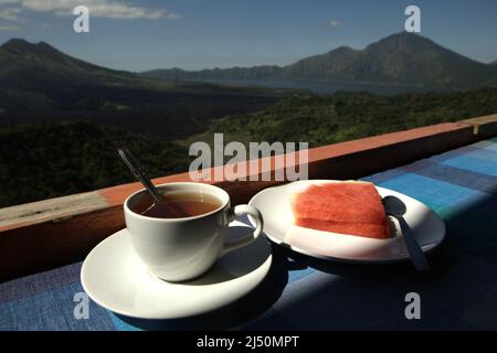 Wassermelone und Tee auf einem Restauranttisch im Hintergrund des Mount Batur in Kintamani, Bangli, Bali, Indonesien. Stockfoto