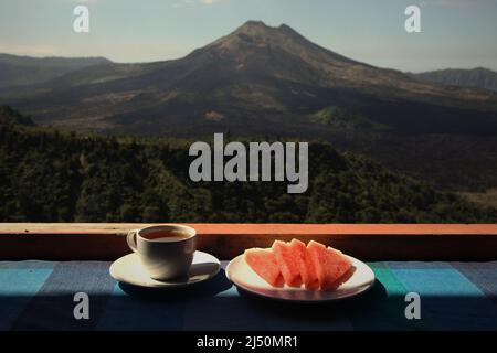 Wassermelone und Tee auf einem Restauranttisch im Hintergrund des Mount Batur in Kintamani, Bangli, Bali, Indonesien. Stockfoto