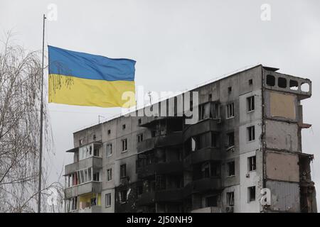 Non Exclusive: BORODIANKA, UKRAINE - 16. APRIL 2022 - Eine ukrainische Flagge fliegt vor einem Wohngebäude, das durch Schellin beschädigt wurde Stockfoto