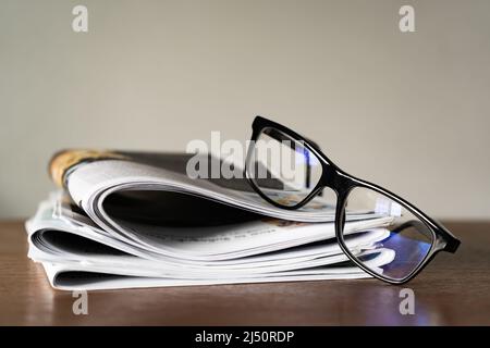 Blaues Licht blockierende Gläser auf Stapel von Zeitungen Stockfoto