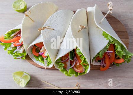 Saftige, leckere Tortillas mit gehacktem frischem Gemüse und Hühnerfilet auf einem hölzernen Küchentisch. Das Konzept des hausgemachten Fast Food Stockfoto