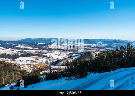 Am Wintertag können Sie die Stadt Mesto mit den Jeseniky-Bergen auf dem Hintergrund des Wanderweges auf dem Kralicky Sneznik-Hügel in Tschechien bewundern Stockfoto