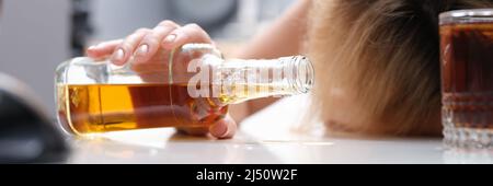 Frau schläft am Tisch mit einer Flasche Alkohol in den Händen in Nahaufnahme Stockfoto