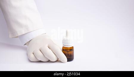 Marihuanaöl in Tropfenspender-Flasche in Handschuhen, weißer Hintergrund Stockfoto